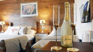 A hotel room with a wooden headboard, a bed with white bedding, two bedside tables with lamps, and a bottle of Freixenet Prosecco on a table. - Ardentorrie Guest House (Inverness)