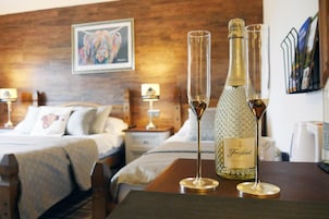 Una habitación de hotel con cabecera de madera, una cama con ropa de cama blanca, dos mesitas de noche con lámparas y una botella de Freixenet Prosecco sobre una mesa.
