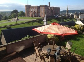 Un patio con una mesa y sillas, una sombrilla y vistas a un edificio que parece un castillo al fondo.