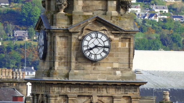 A clock tower with a large clock face, stone architecture, and a view of houses in the background. - Ardentorrie Guest House (Inverness)