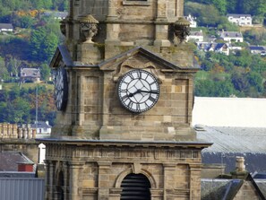 A clock tower with a large clock face, stone architecture, and a view of houses in the background.