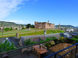 Vista de un edificio histórico con un patio, un área de comedor con mesas al aire libre y un cielo azul despejado.