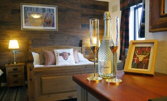 Habitación de hotel con cabecera de madera, cama con almohadas, un cuadro enmarco de un toro y dos botellas de Prosecco sobre una mesa de madera.
