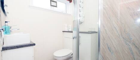 A bathroom with a white toilet, a sink with a soap dispenser, a glass shower enclosure, and a marble wall.