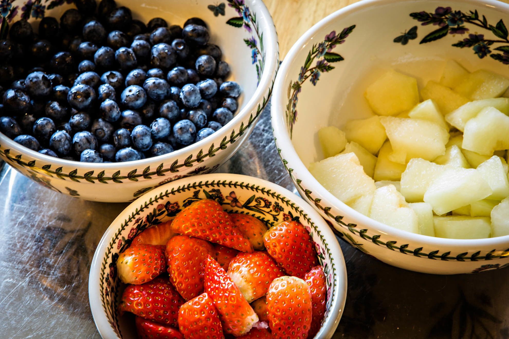 Three bowls with different fruits: blueberries, strawberries, and diced apples.