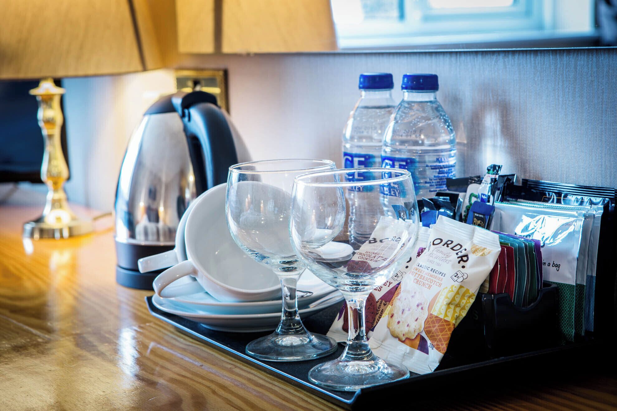 A tray with glasses, plates, water bottles, and a bag of cookies on a wooden table.