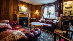 A cozy living room with leather sofas, a fireplace, a wooden floor, and a bookshelf. - Orchard Lodge & Wolds Restaurant (Scarborough)