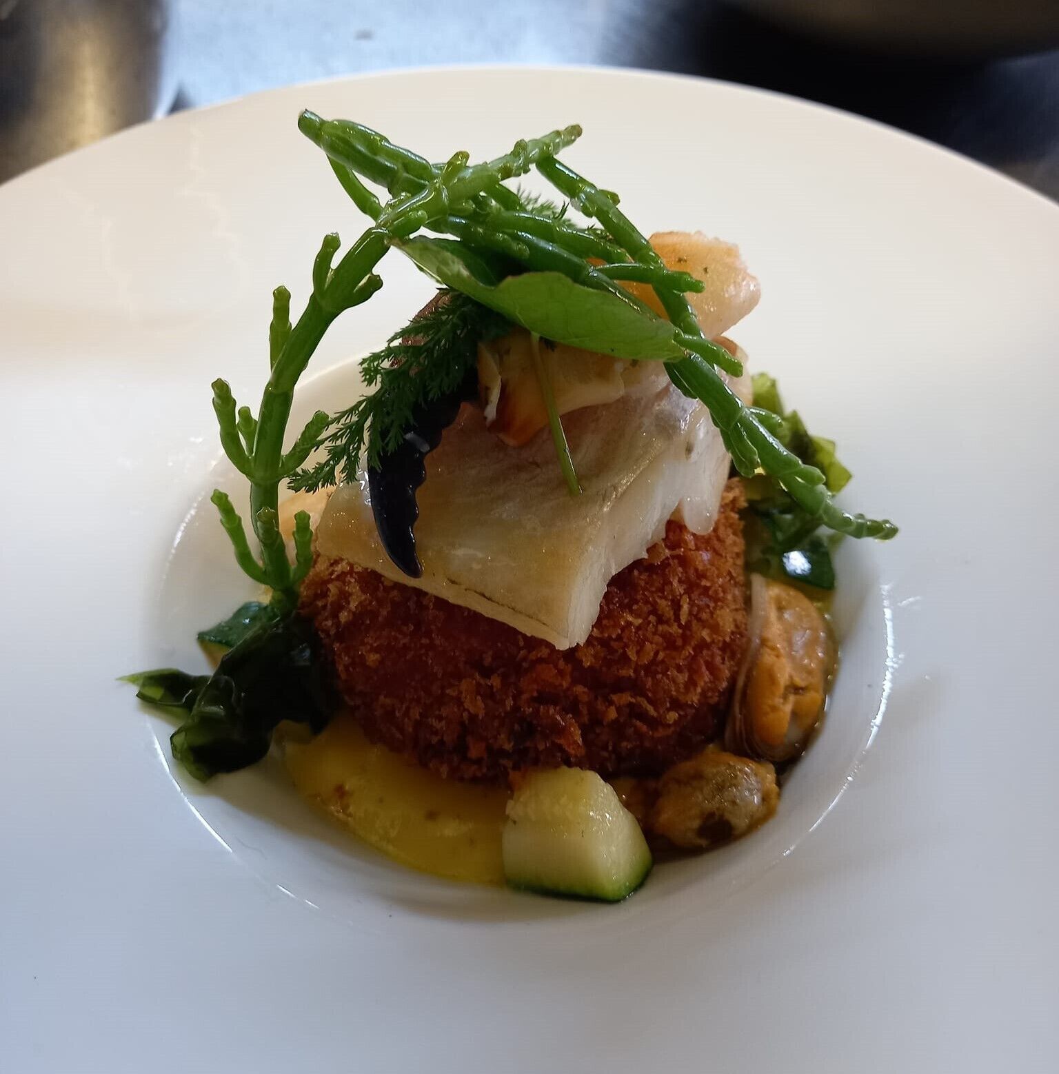 A dish with a crispy base, topped with a creamy element and garnished with green herbs.