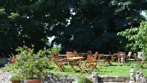 An outdoor seating area with wooden tables and chairs, surrounded by potted plants and a stone wall. - Orchard Lodge & Wolds Restaurant (Scarborough)