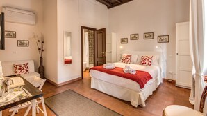 A bedroom with a large bed, a wooden ceiling, a dining table, and a white sofa. - Piccolo Trevi Suites (Rome)