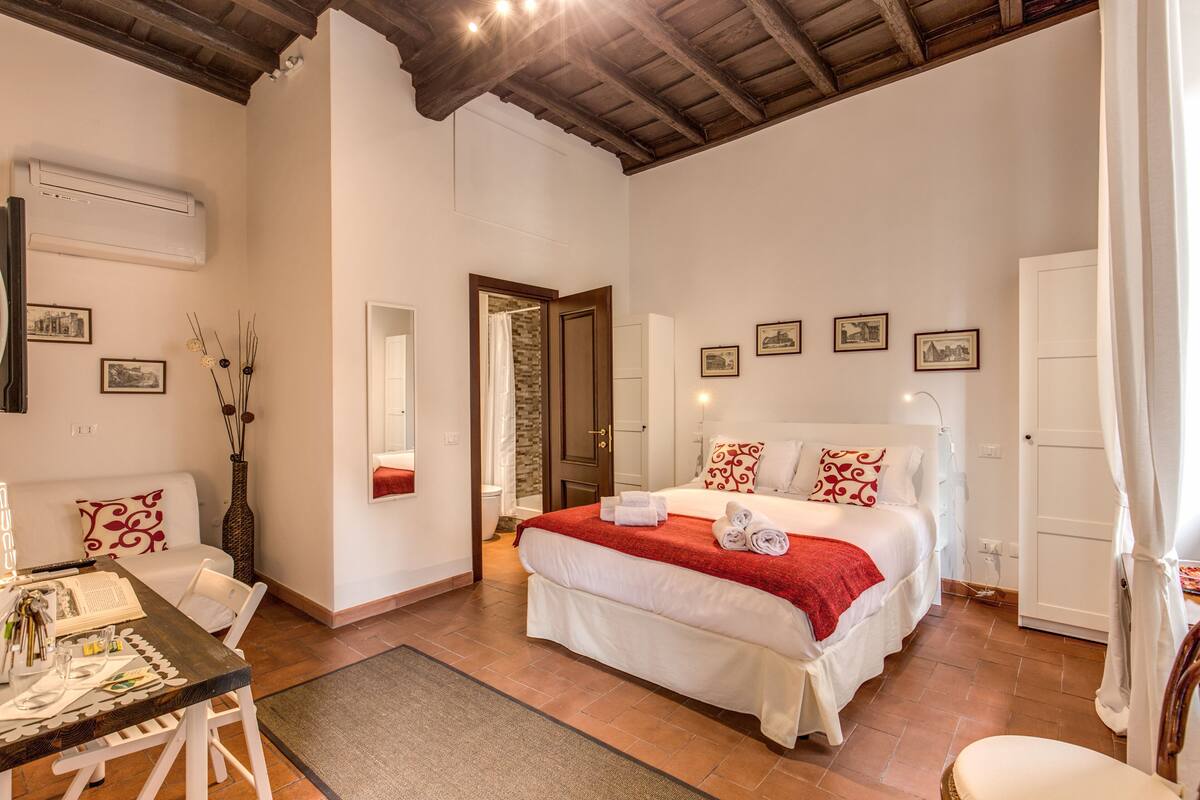 Un dormitorio con una cama grande, techo de madera, una mesa de comedor y un sofá blanco.