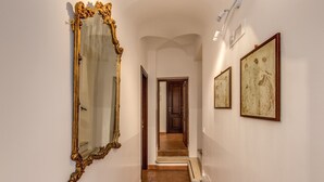 A hallway with a grand mirror, a staircase, and framed artwork on the walls. - Piccolo Trevi Suites (Rome)
