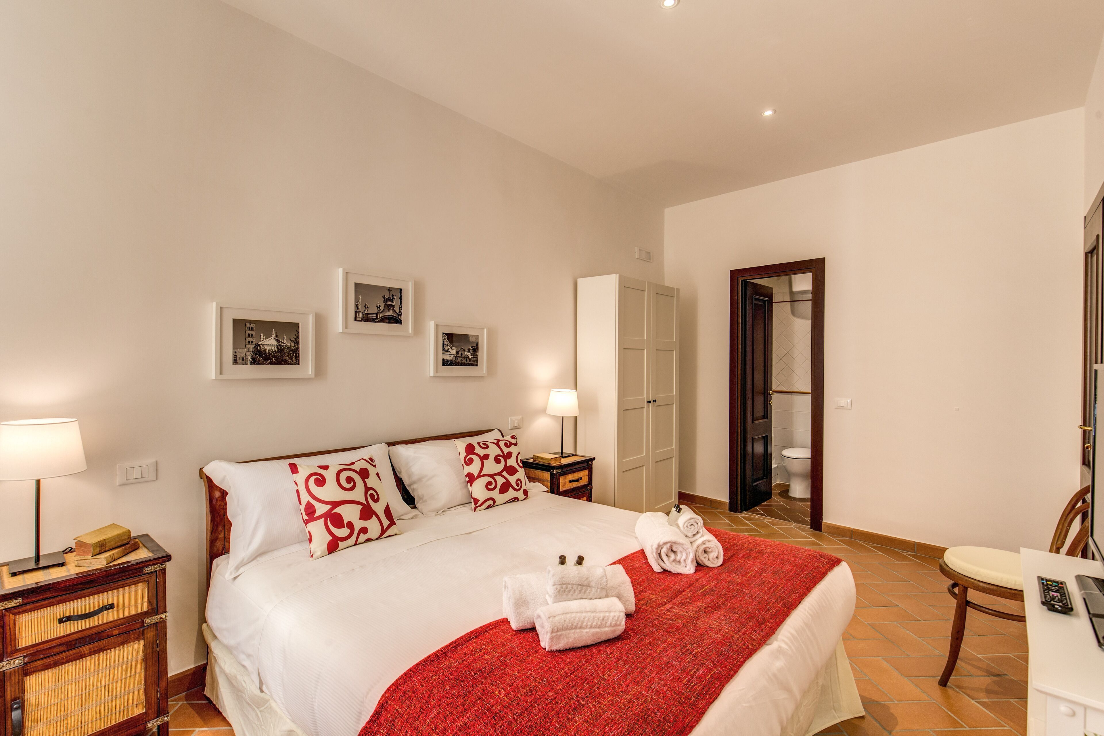 A hotel room with a large bed, a bedside table with a lamp, a wardrobe, and a bathroom visible through an open door.