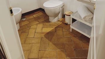 A bathroom with a toilet, sink, and a small shelf with towels.