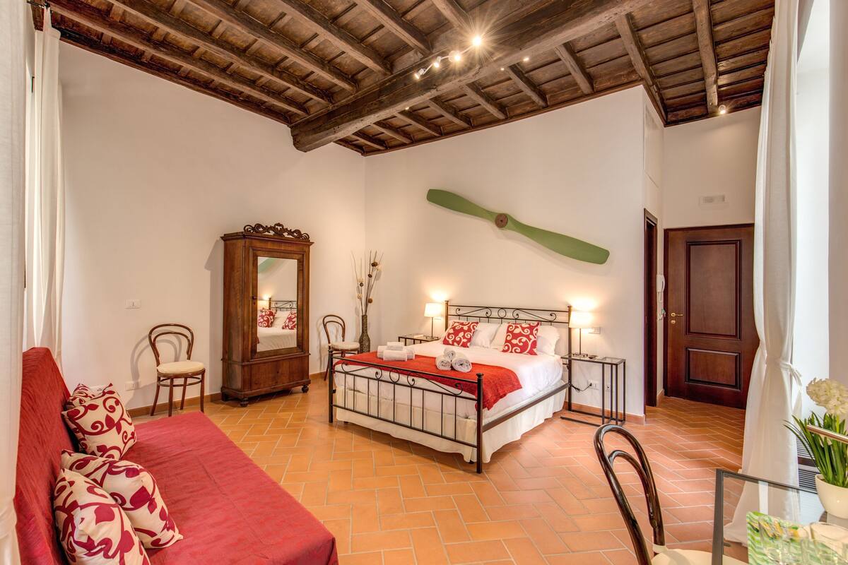 Un dormitorio con cama, una silla de madera, un espejo, una mesita de noche y una puerta.