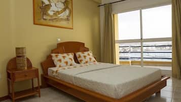 Un dormitorio con una cama grande, una mesita de noche, un cuadro en la pared y una ventana con cortinas.