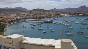 Uma marina com muitos barcos atracados, cercada por um horizonte costeiro com montanhas ao fundo.