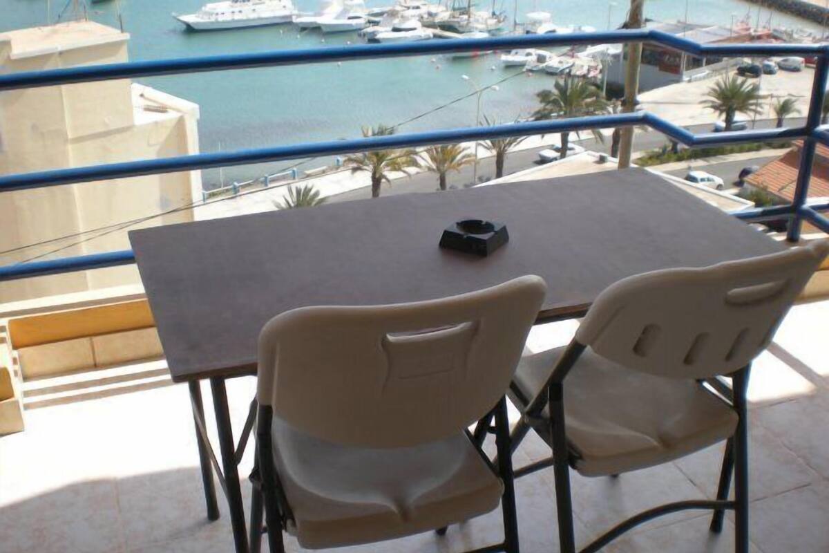 A balcony with a table and two chairs, overlooking a marina with boats.