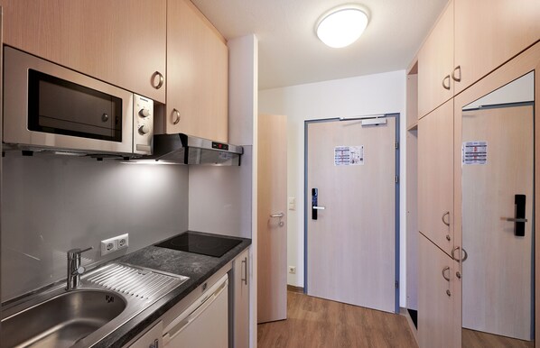 A modern kitchen with a built-in microwave, oven, and stainless steel sink. - Hotel Kolpinghaus Wien Zentral (Vienna)