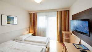A hotel room with two beds, a television, a desk, and a window with curtains. - Hotel Kolpinghaus Wien Zentral (Vienna)