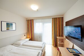 Een hotelkamer met twee bedden, een televisie, een bureau en een raam met gordijnen.
