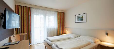 A hotel room with two beds, a desk, a TV, and a window with curtains.