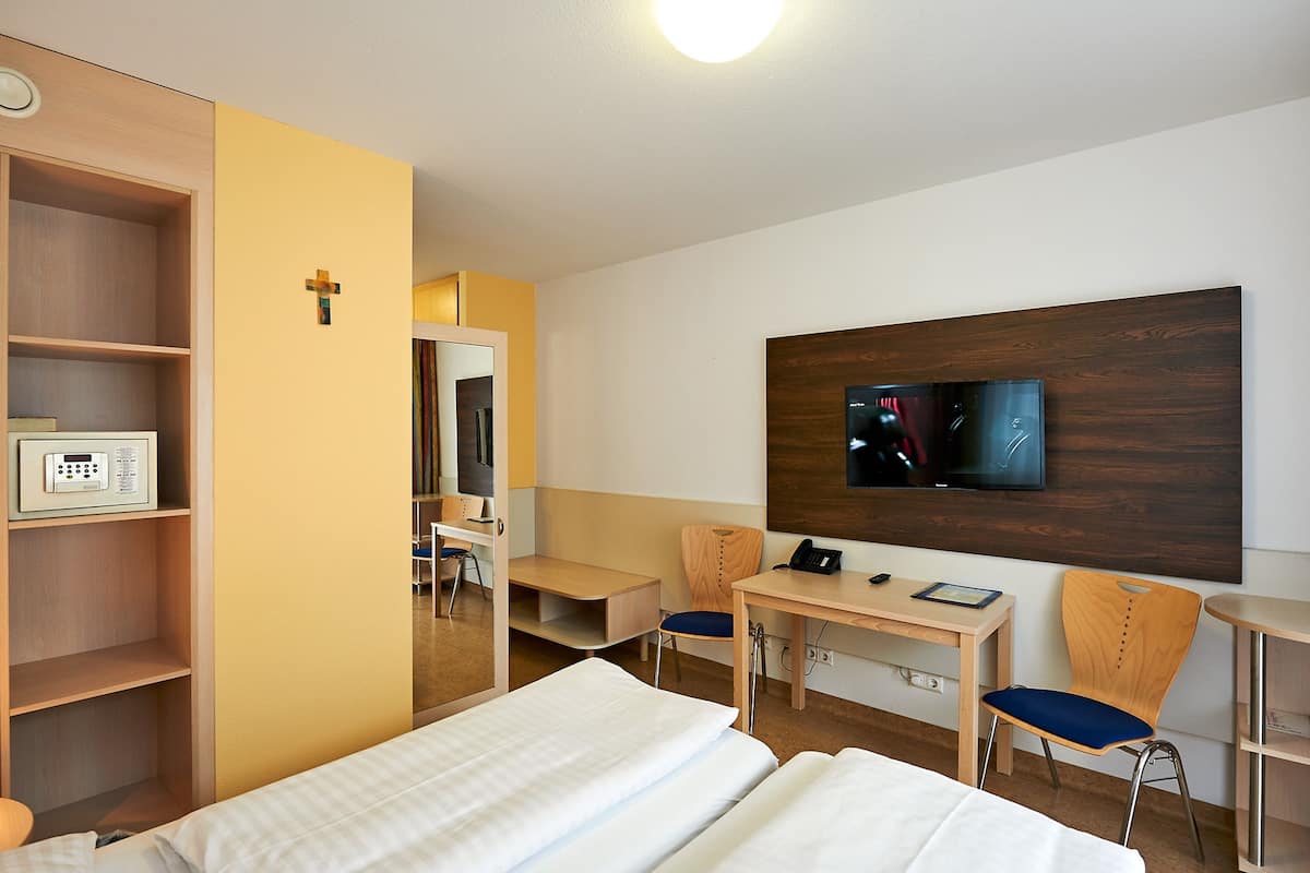 Ein Hotelzimmer mit einem Bett, einem Schreibtisch mit Stuhl, einem an der Wand befestigten Fernseher und einem Kleiderschrank.