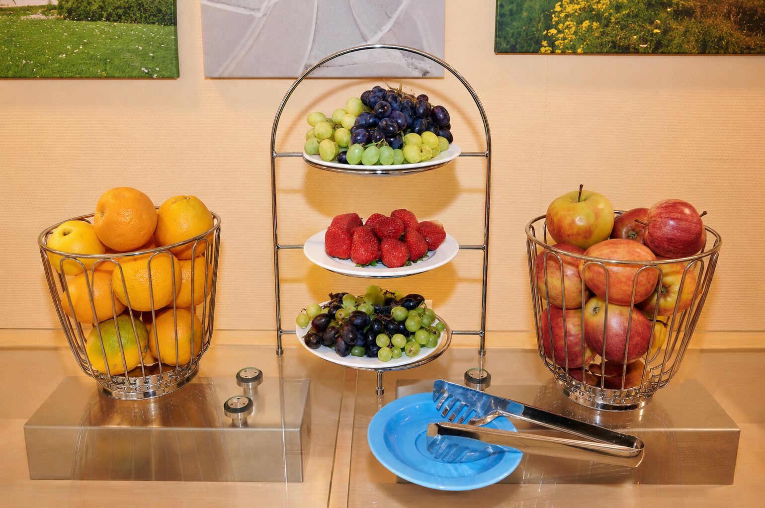 A buffet setup with fruit bowls and a blue plate with tongs.