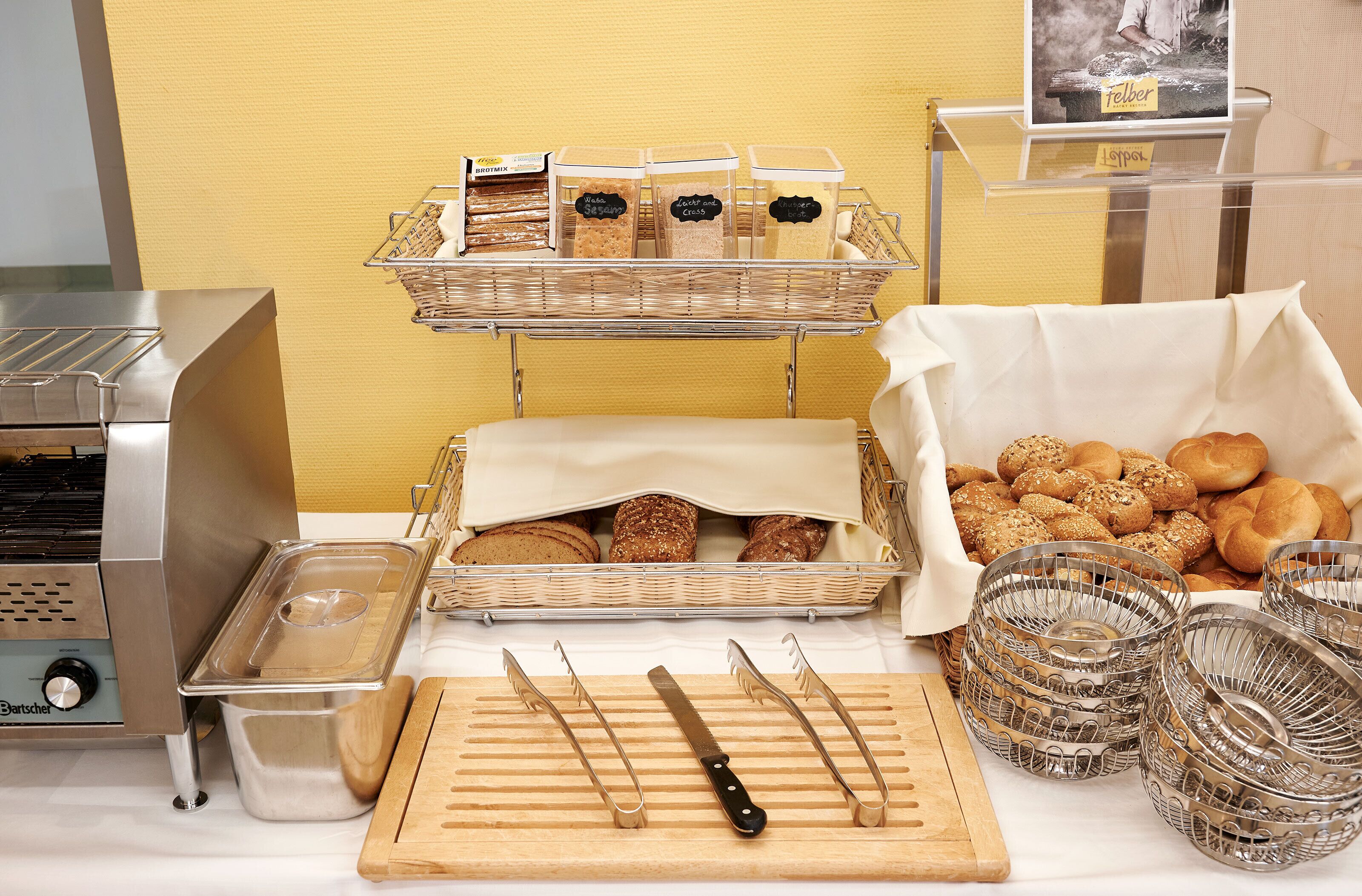 A buffet setup with bread, pastries, and condiments.