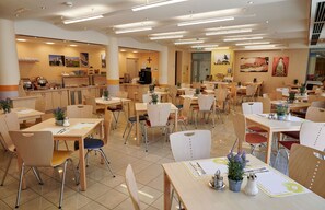 Un'ampia sala da pranzo con diversi tavoli e sedie, un angolo caffè e un bancone con macchina da caffè.