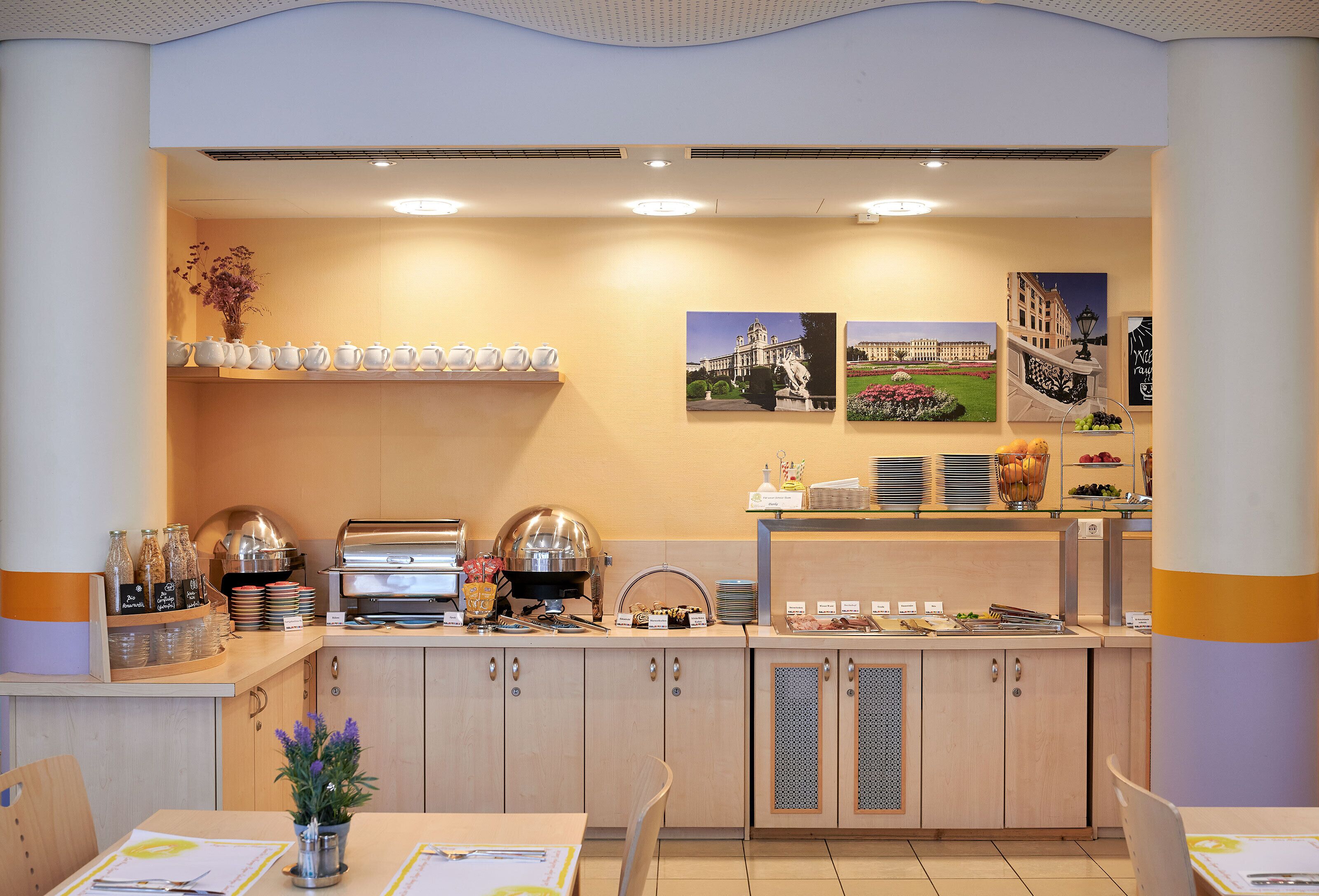 A breakfast buffet area with tea sets, a coffee machine, and a fruit display.
