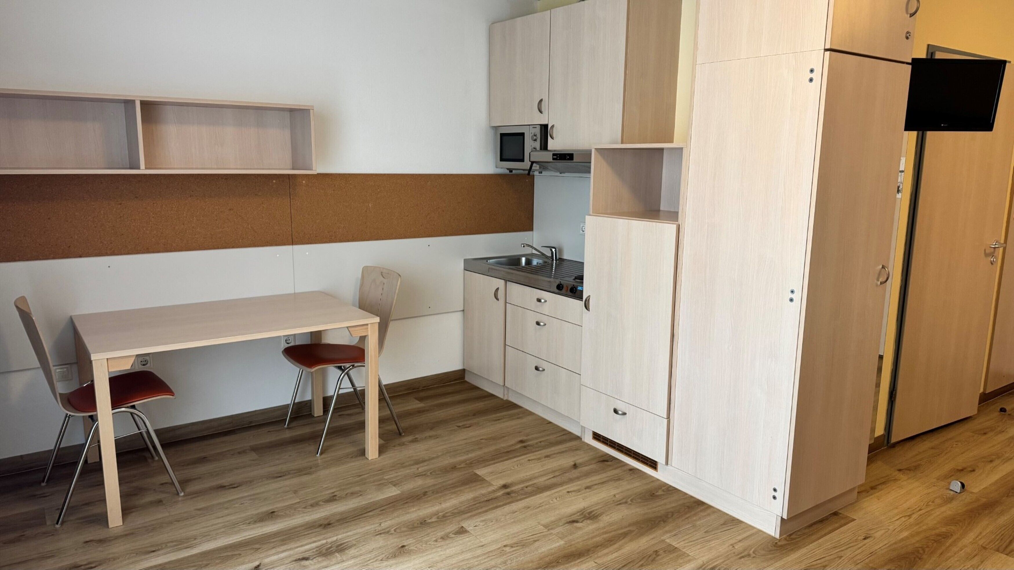 Eine kompakte Küche mit einem Holztisch, zwei Stühlen, einer Mikrowelle und einem eingebauten Backofen.