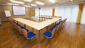 A conference room with a long table, blue chairs, a whiteboard, and a projector screen. - Hotel Kolpinghaus Wien Zentral (Vienna)