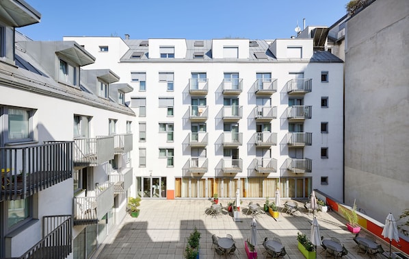 A multi-story residential building with balconies, a courtyard with outdoor seating, and a clear sky.