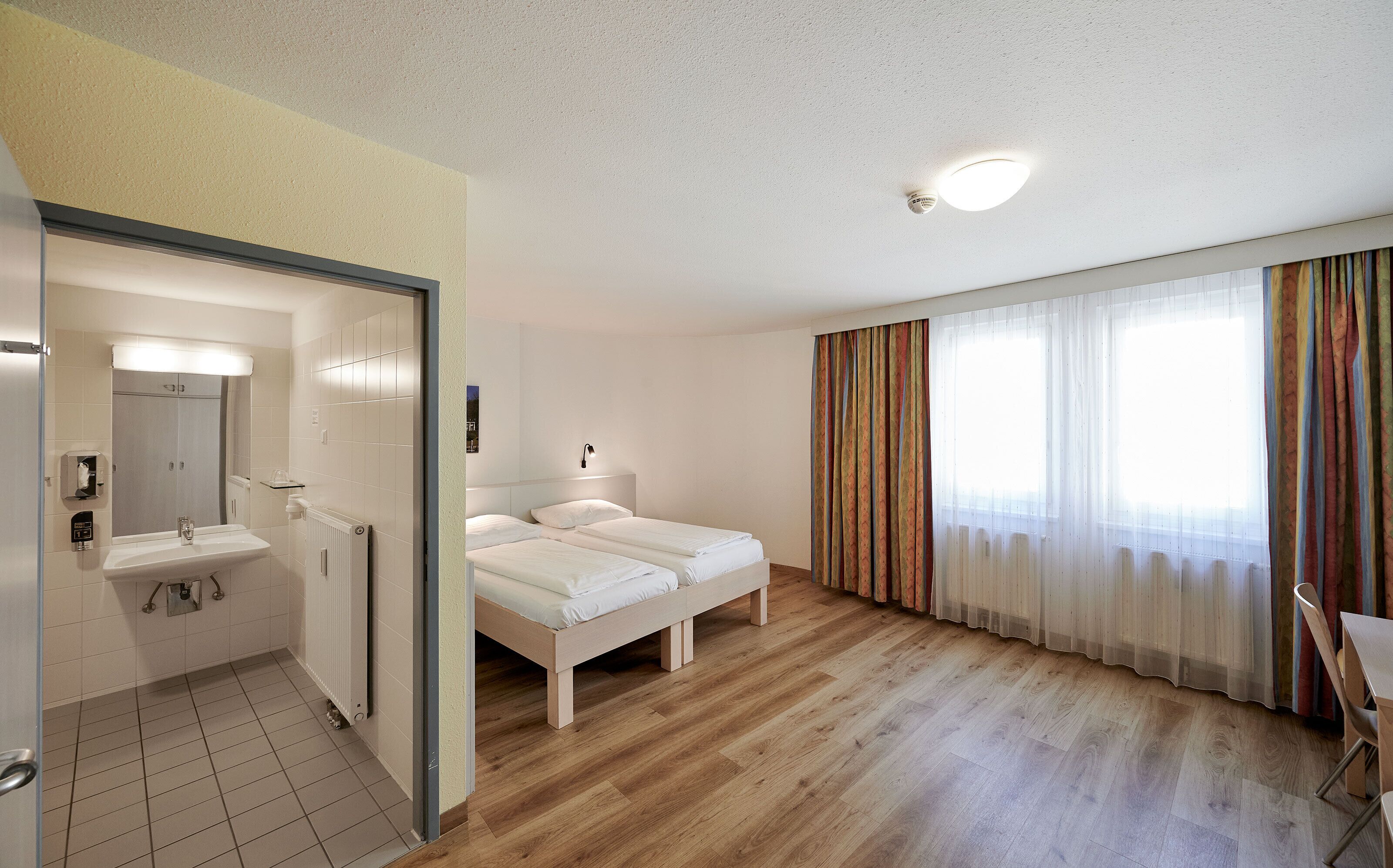 Une chambre d’hôtel avec une salle de bain, un lit et une fenêtre avec des rideaux.
