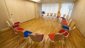A conference room with a wooden floor, arranged chairs in a semi-circle, and a projector on the ceiling. - Hotel Kolpinghaus Wien Zentral (Vienna)