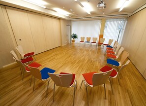 Een vergaderruimte met een houten vloer, stoelen zijn in een halve cirkel opgesteld, en een beamer aan het plafond.