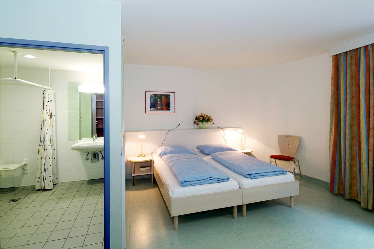 Ein Hotelzimmer mit Bett, Nachttischen, einem Sessel, einem Spiegel, einem Waschbecken und einer Duschkabine.