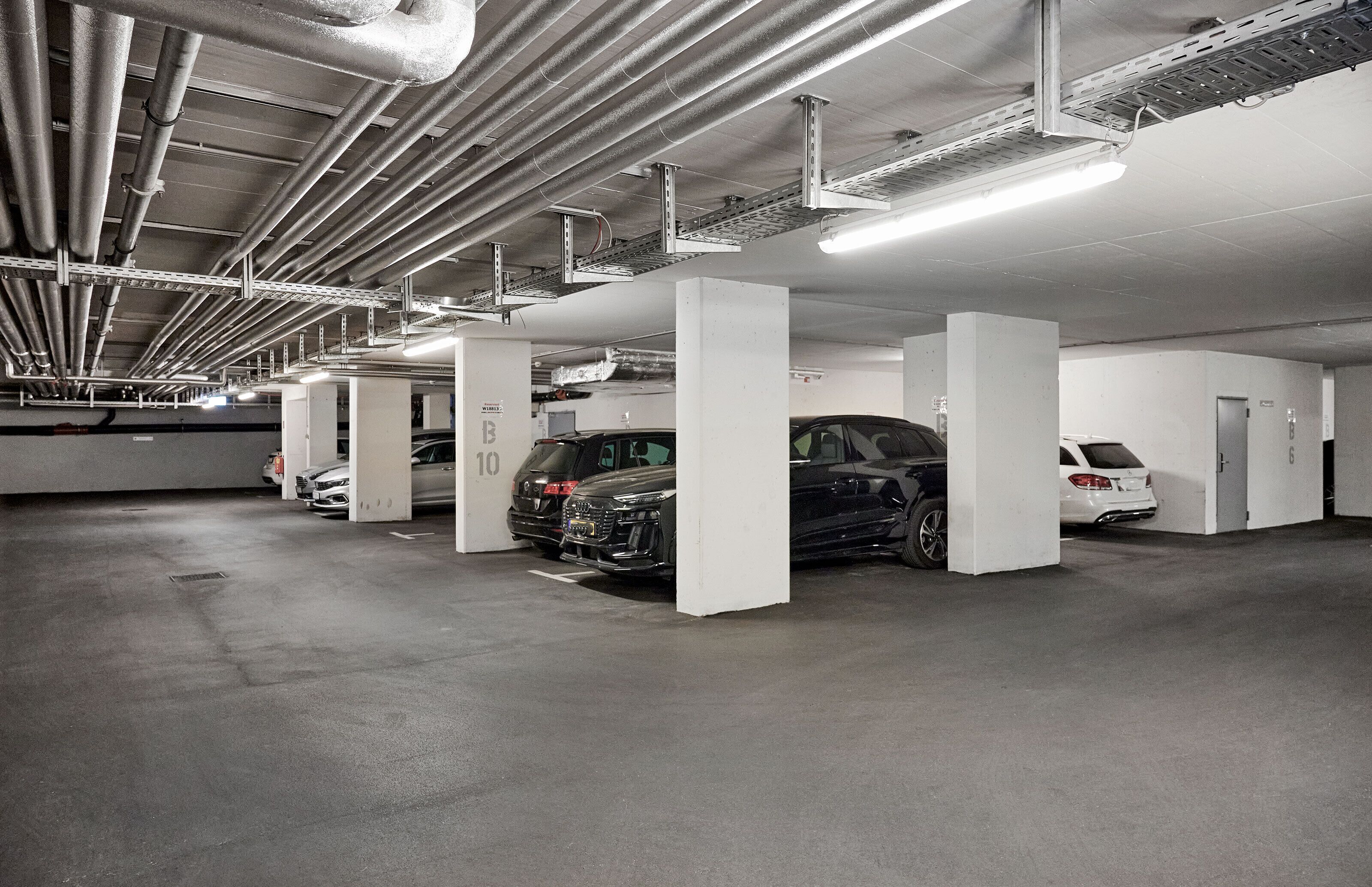 Un estacionamiento subterráneo de varios niveles, con pilares blancos y señalización clara que indica los espacios de estacionamiento.