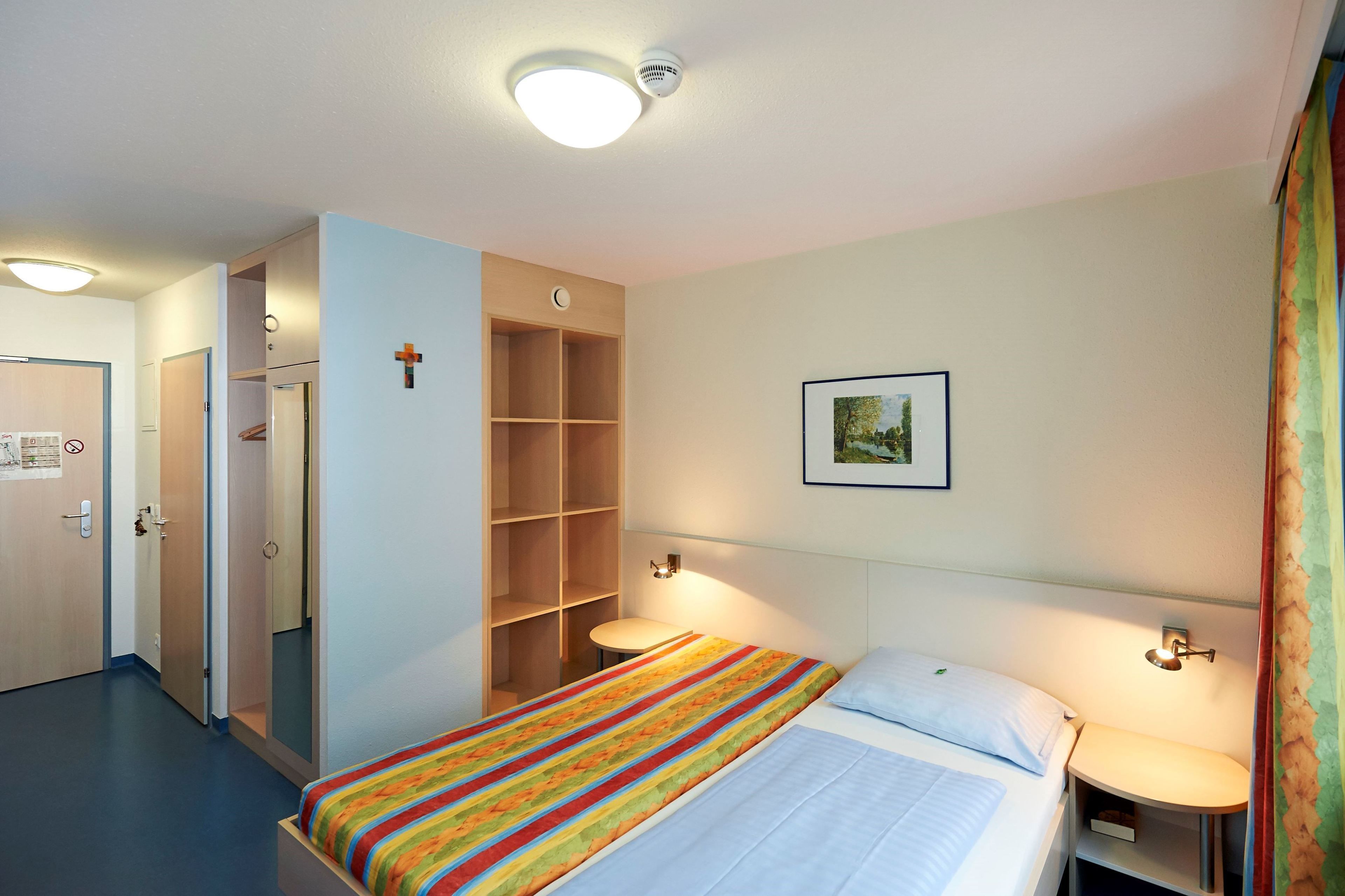 Una habitación de hotel con cama, mesitas de noche, armario y un cuadro en la pared.