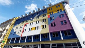Ein mehrgeschossiges Gebäude mit einer farbenfrohen Fassade, welche gelbe, blaue, violette und weiße Elemente kombiniert.