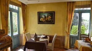 Comedor con una mesa preparada para dos personas, un cuadro en la pared y ventanas amplias con cortinas.