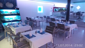 A restaurant with tables set for dining, a fish tank, and a modern interior design. - Neptune Hotel Apartments (Pegeia)