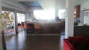 A spacious living area with a red sofa, a kitchen area with a bar, and a dining area with chairs and a table. - Neptune Hotel Apartments (Pegeia)