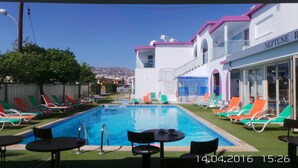 A swimming pool area with lounge chairs and tables, a sign indicating a swimming pool, and a building with a sign reading "NEPTUNE R". - Neptune Hotel Apartments (Pegeia)