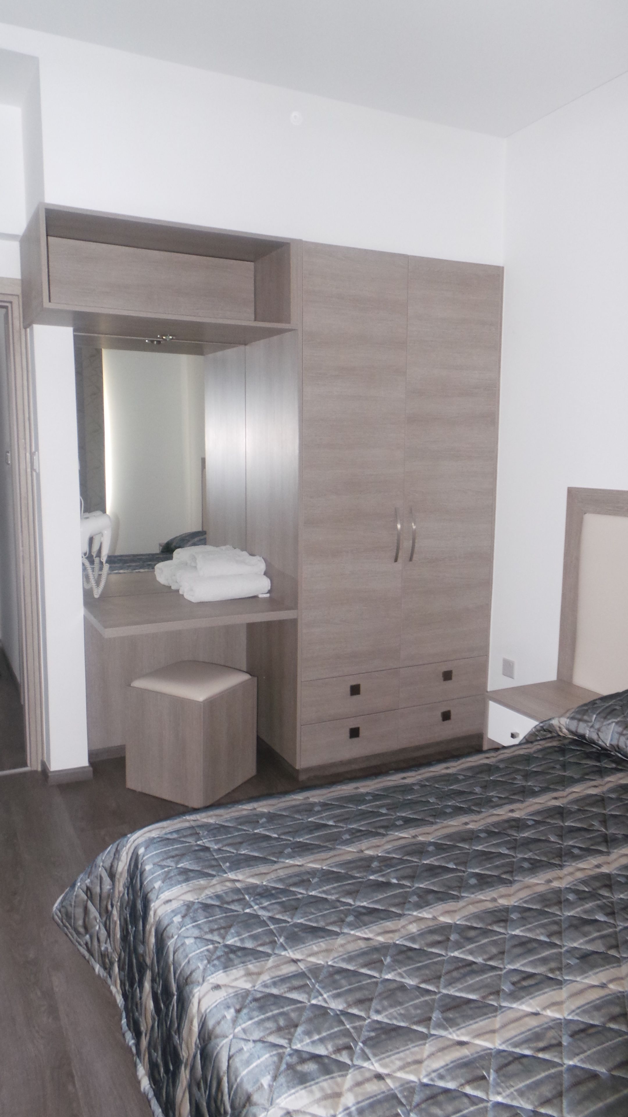 A bedroom with a bed, a wardrobe, a vanity with a mirror, and a small stool.