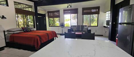 A modern room with a bed, a sofa, a dining table, and a kitchen area.