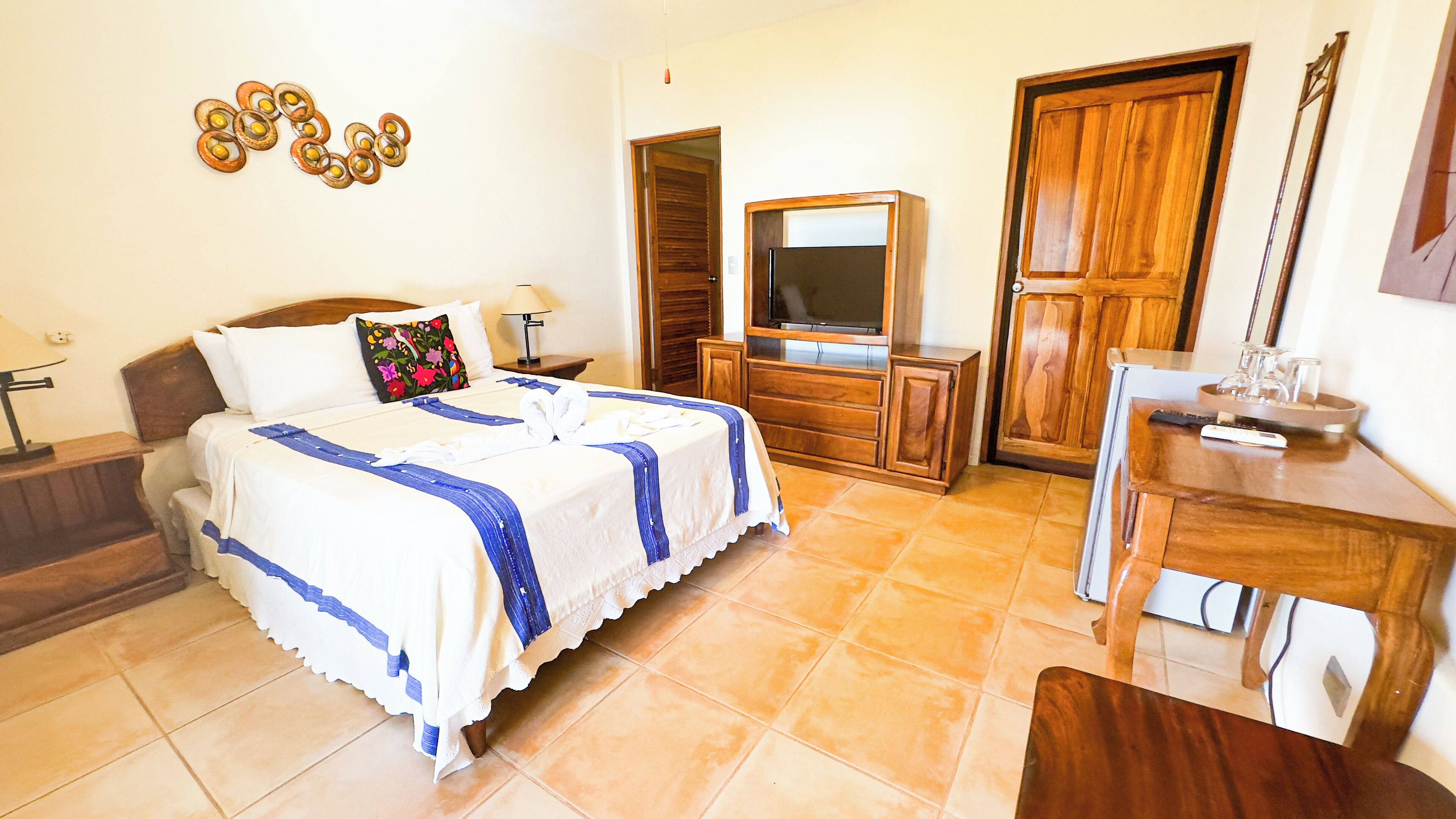 Une chambre d’hôtel avec un lit, une télévision, une commode en bois et un bureau.