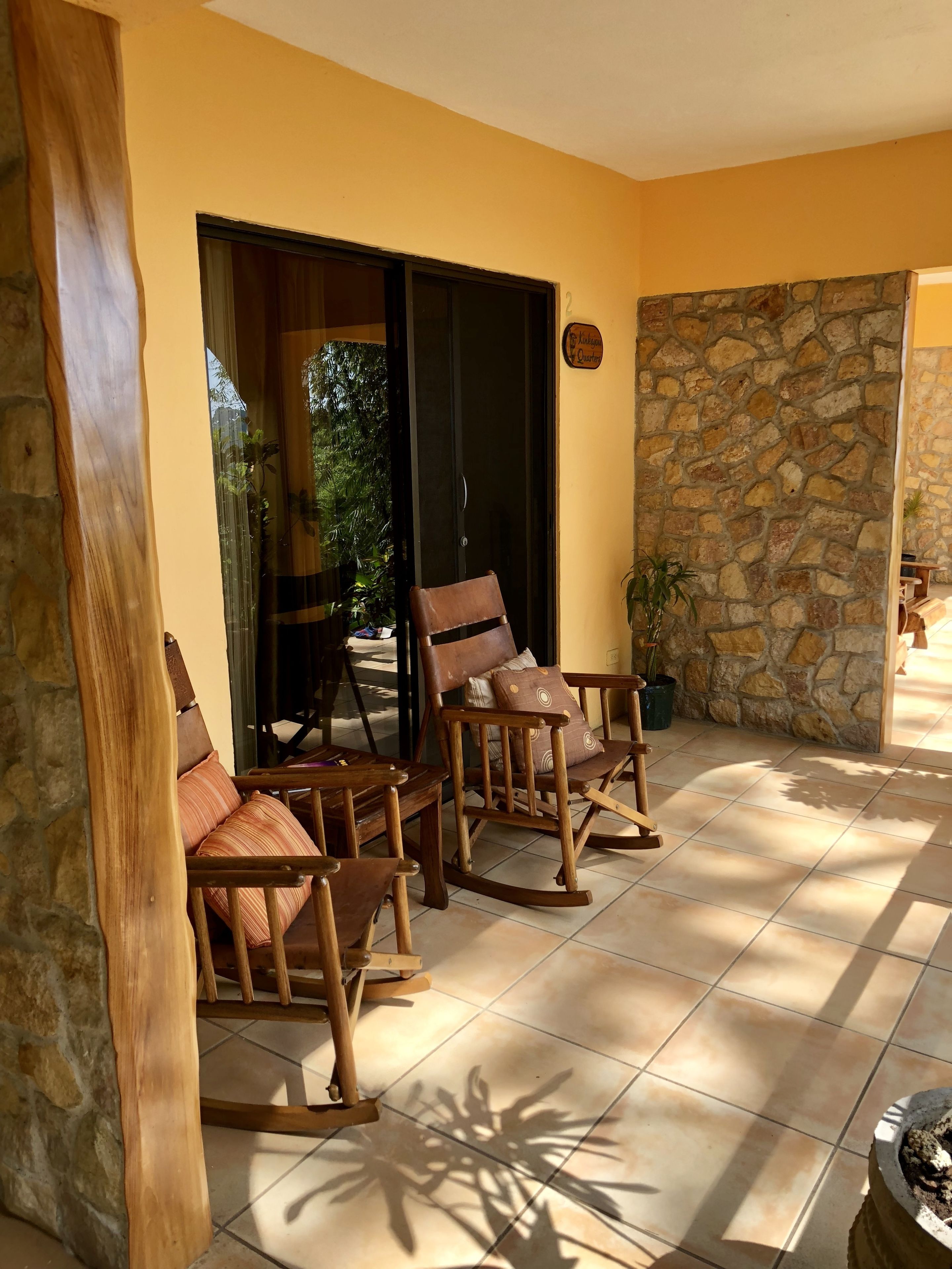 A patio area with wooden rocking chairs and a table, stone walls, and a glass door leading outside.