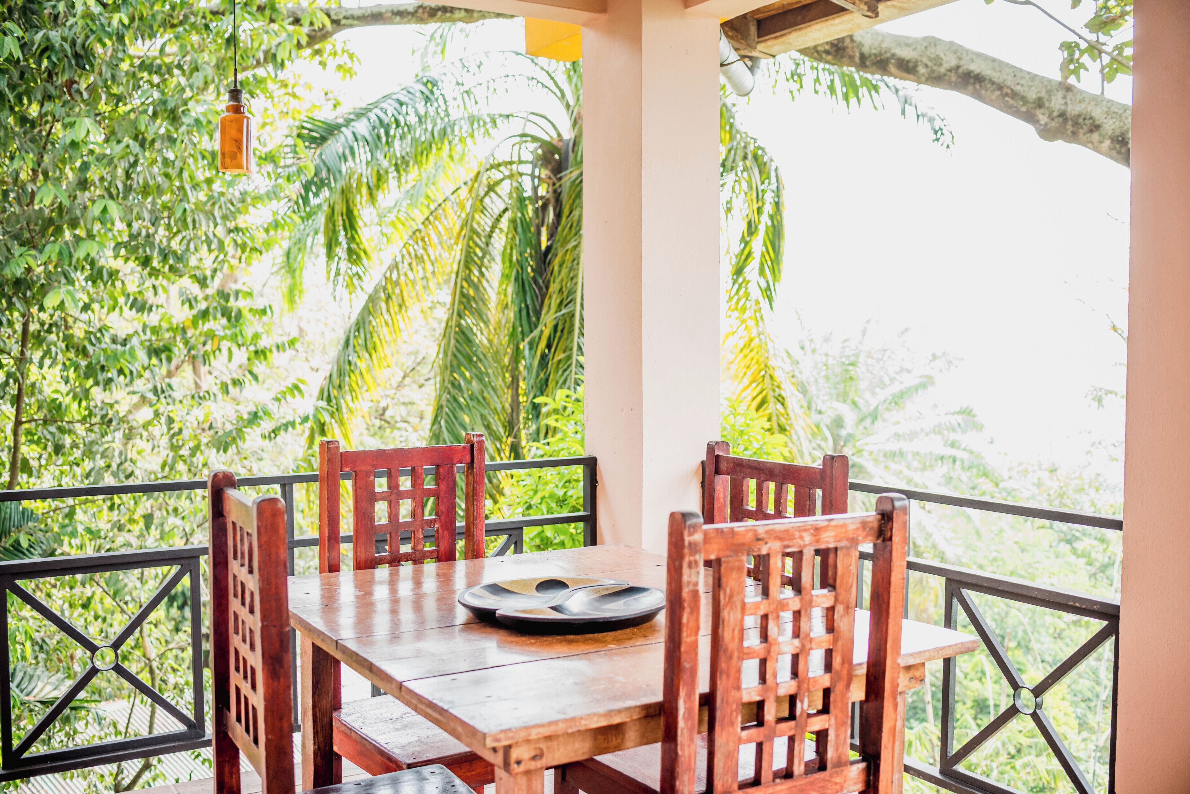 Une table en bois, entourée de chaises, sur un balcon offrant une vue sur la végétation tropicale.